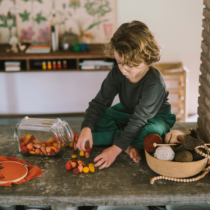 Child playing with colorful wooden shapes on a table in a room with decorative elements.