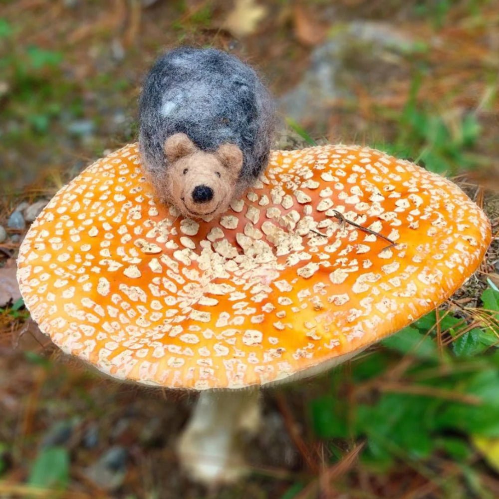 Felted hedgehog sitting on a yellow and orange mushroom in a nature setting