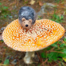 Felted hedgehog sitting on a yellow and orange mushroom in a nature setting