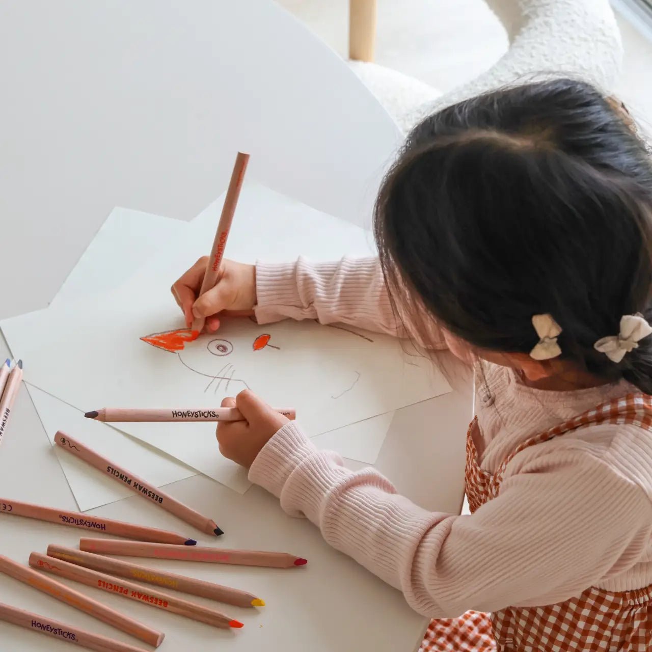 Child coloring a picture with colored pencils on a white surface