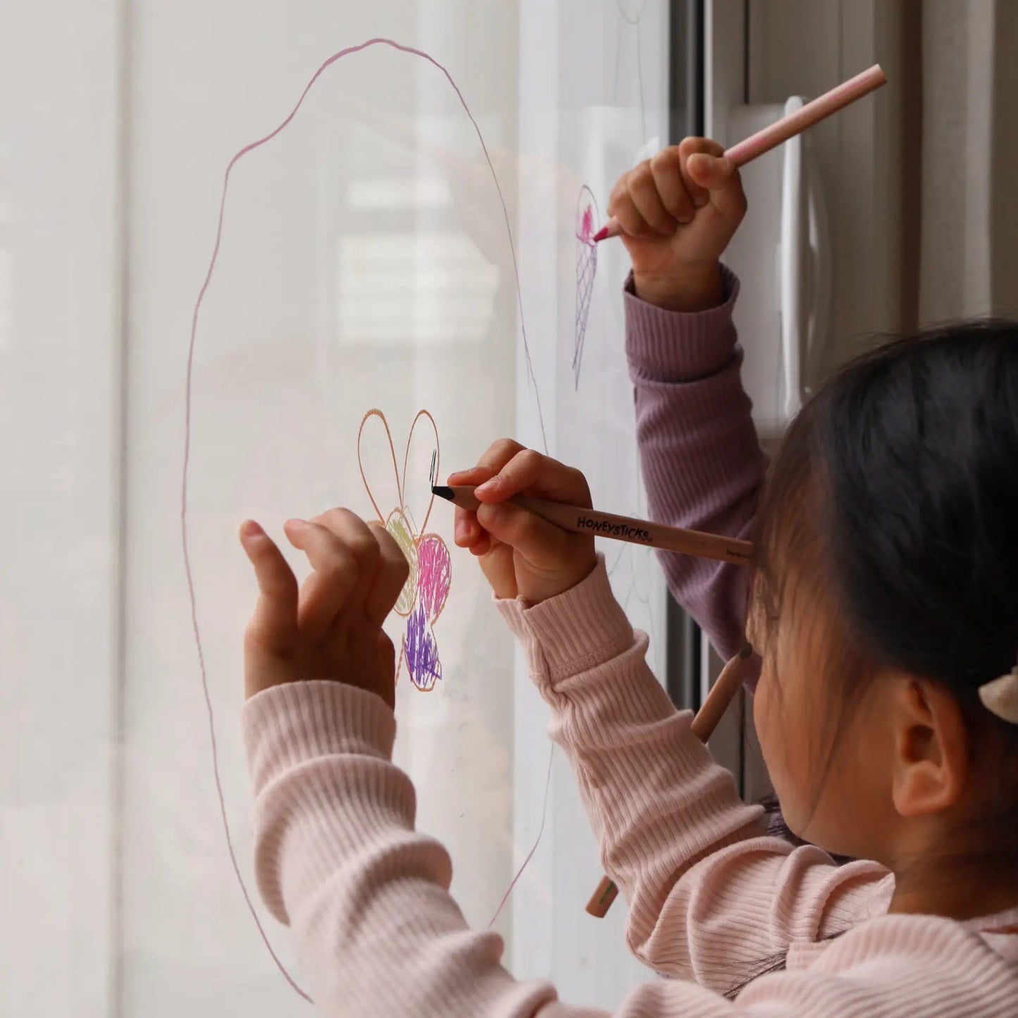 Two children drawing on a glass window with colorful pencils
