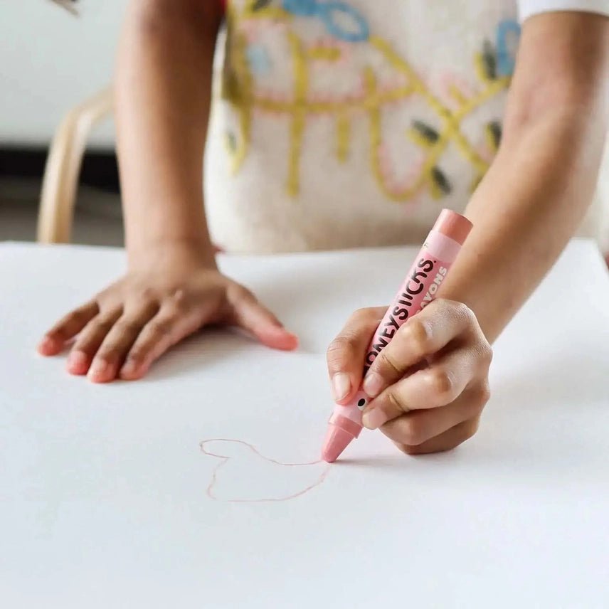 Child's hand holding a pink crayon drawing on a white surface.