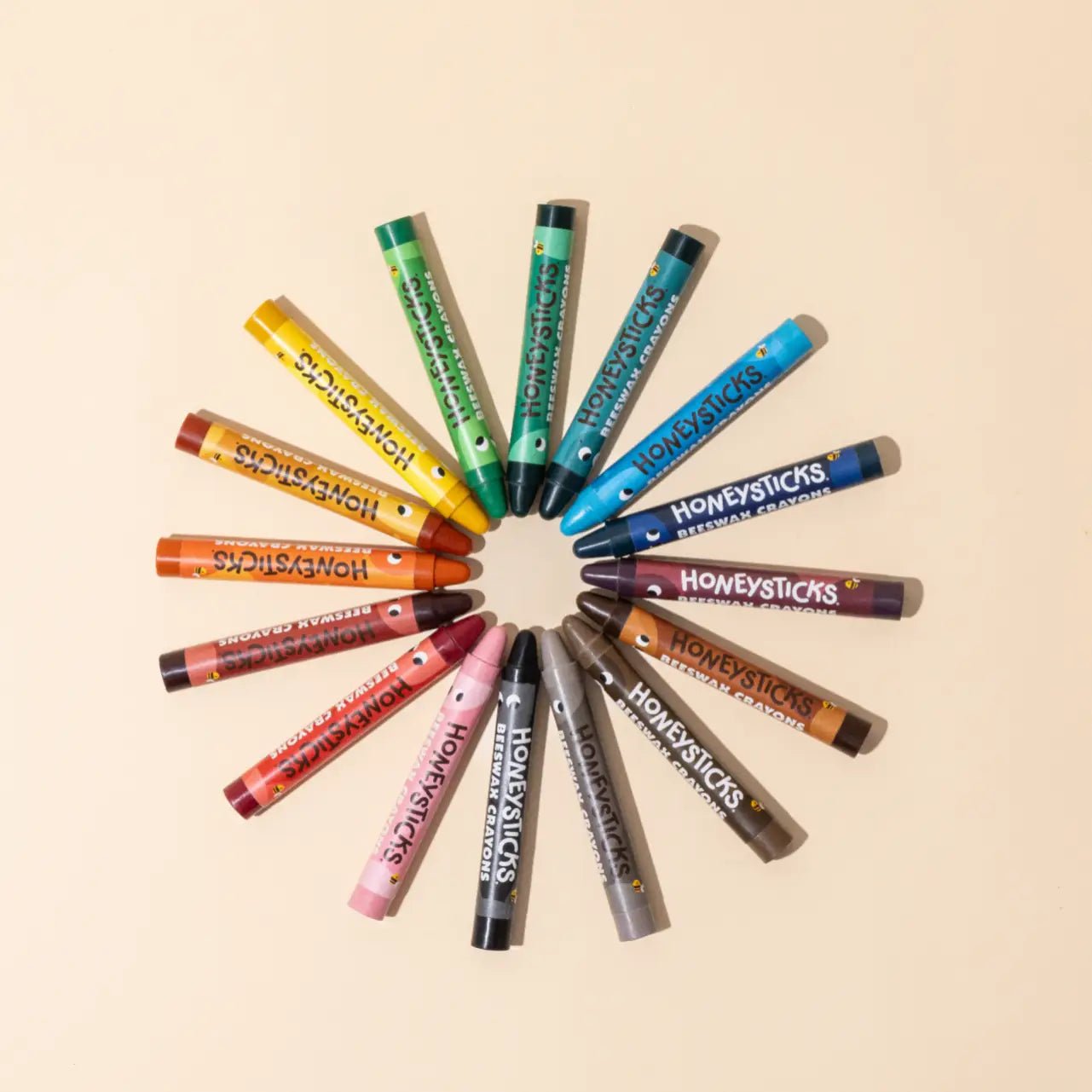 16 Honeysticks crayons in assorted colors arranged in a circular pattern on a light beige background.