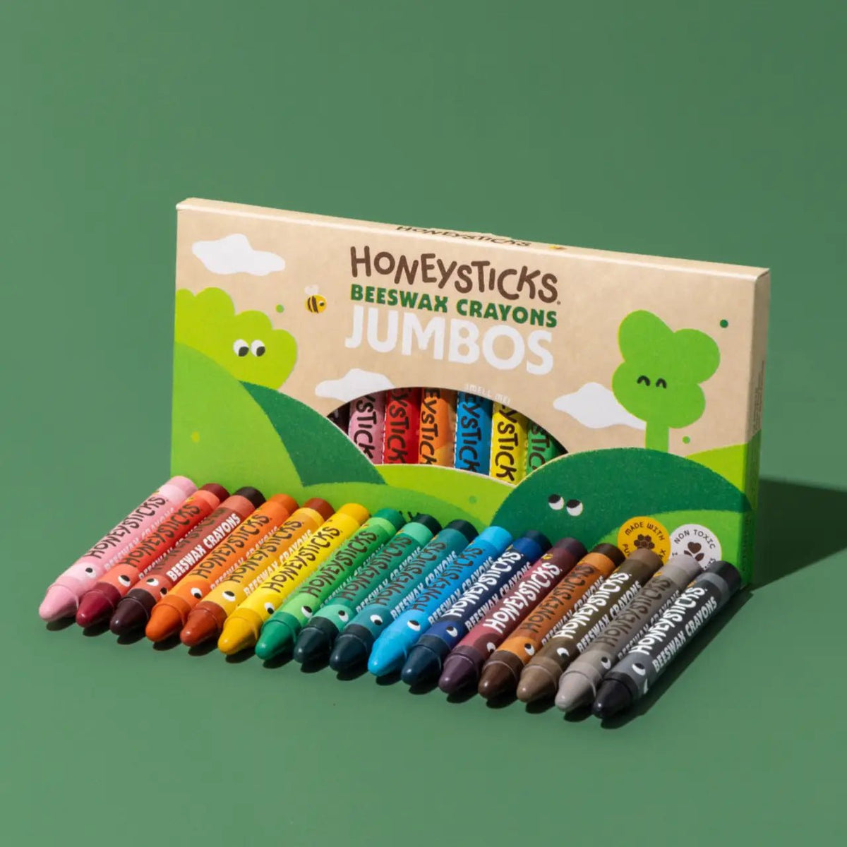 A box of Honeysticks Beeswax Crayons Jumbos with multiple colorful crayons arranged in front on a solid green background.