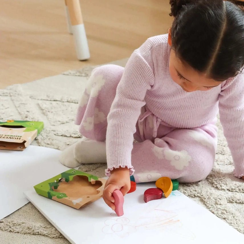 Child sitting on a rug coloring with petal-shaped crayons