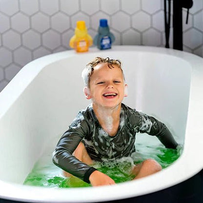 Child in a bathtub with green water and Honeysticks bubble bath products on the edge.