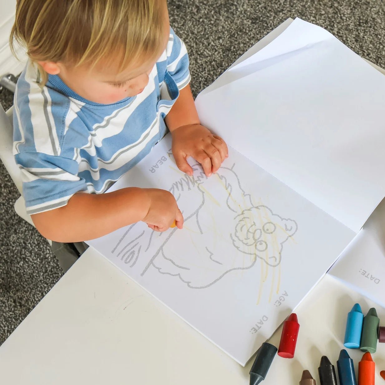 Child sitting at a table with a coloring book and crayons