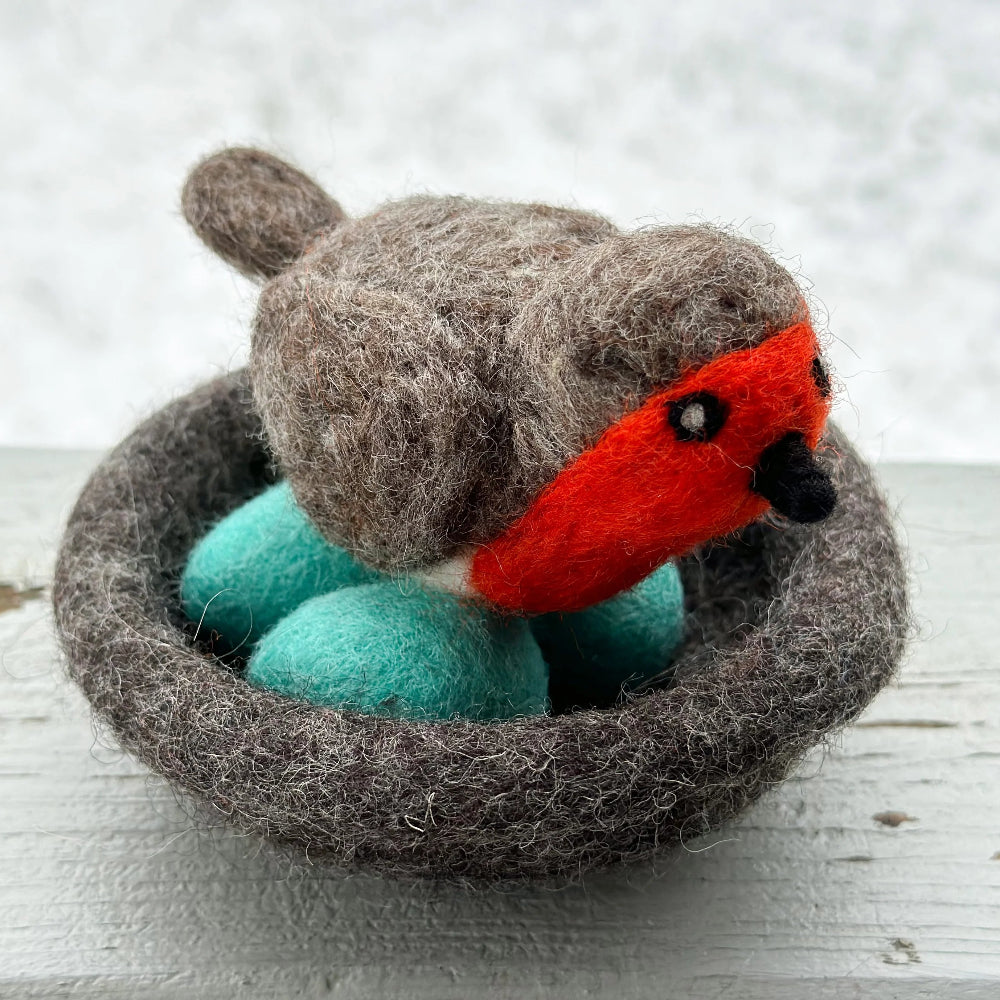 Felted toy robin bird in a nest on a wooden surface