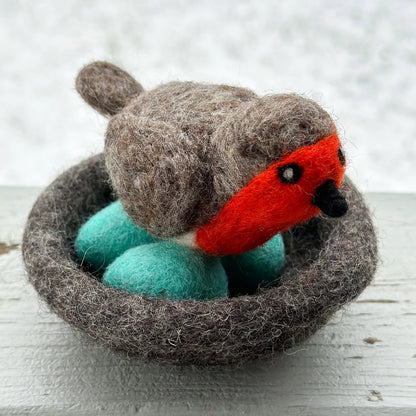 Felted toy robin bird in a nest on a wooden surface
