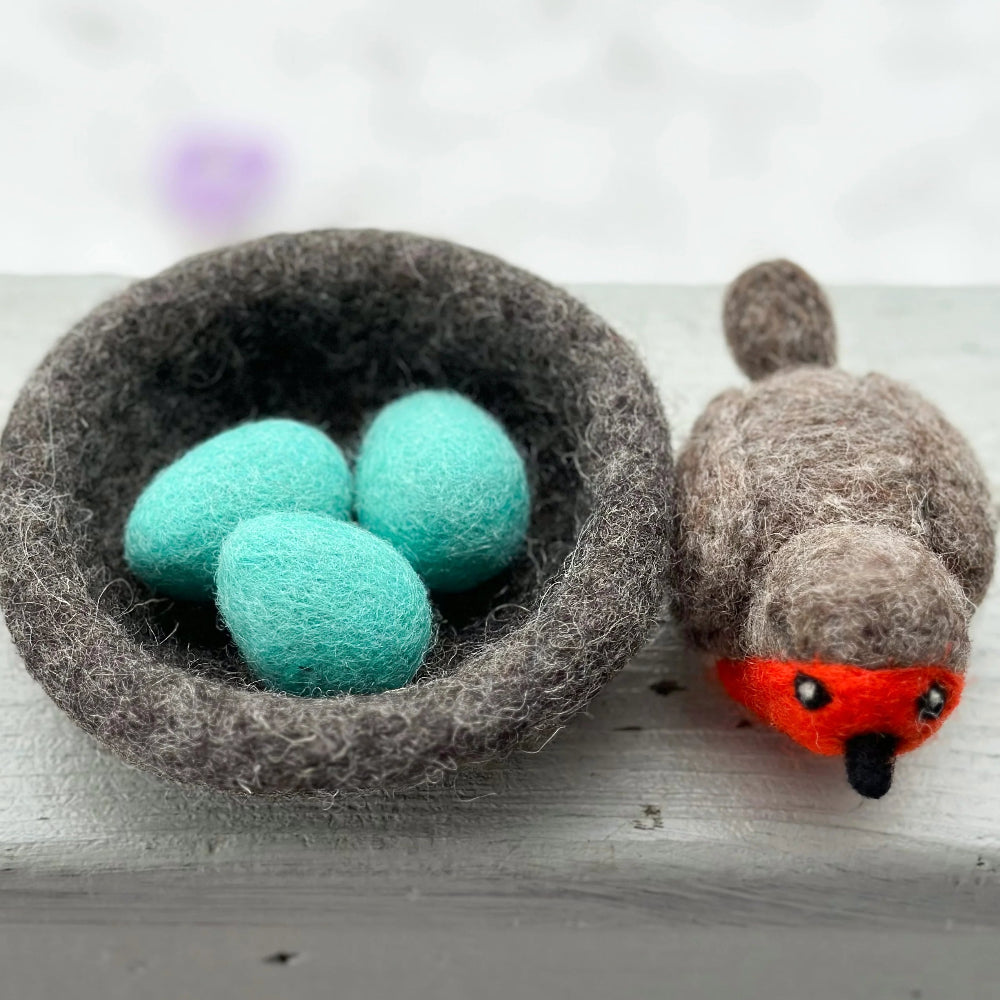 Felted nest with turquoise eggs and a felted robin with red face on a white surface