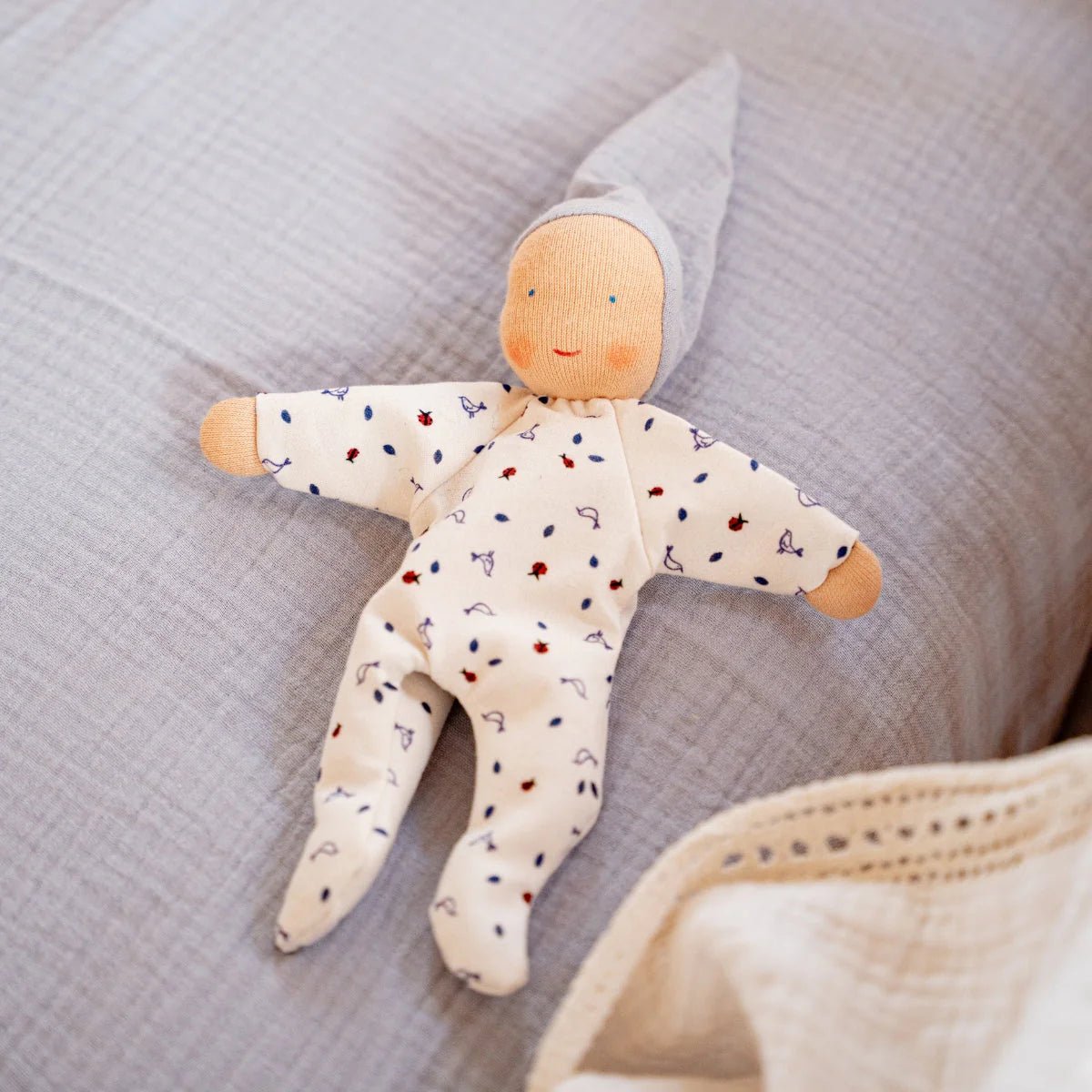 Organic cotton baby doll with a blue sleeping cap on a light blue fabric surface