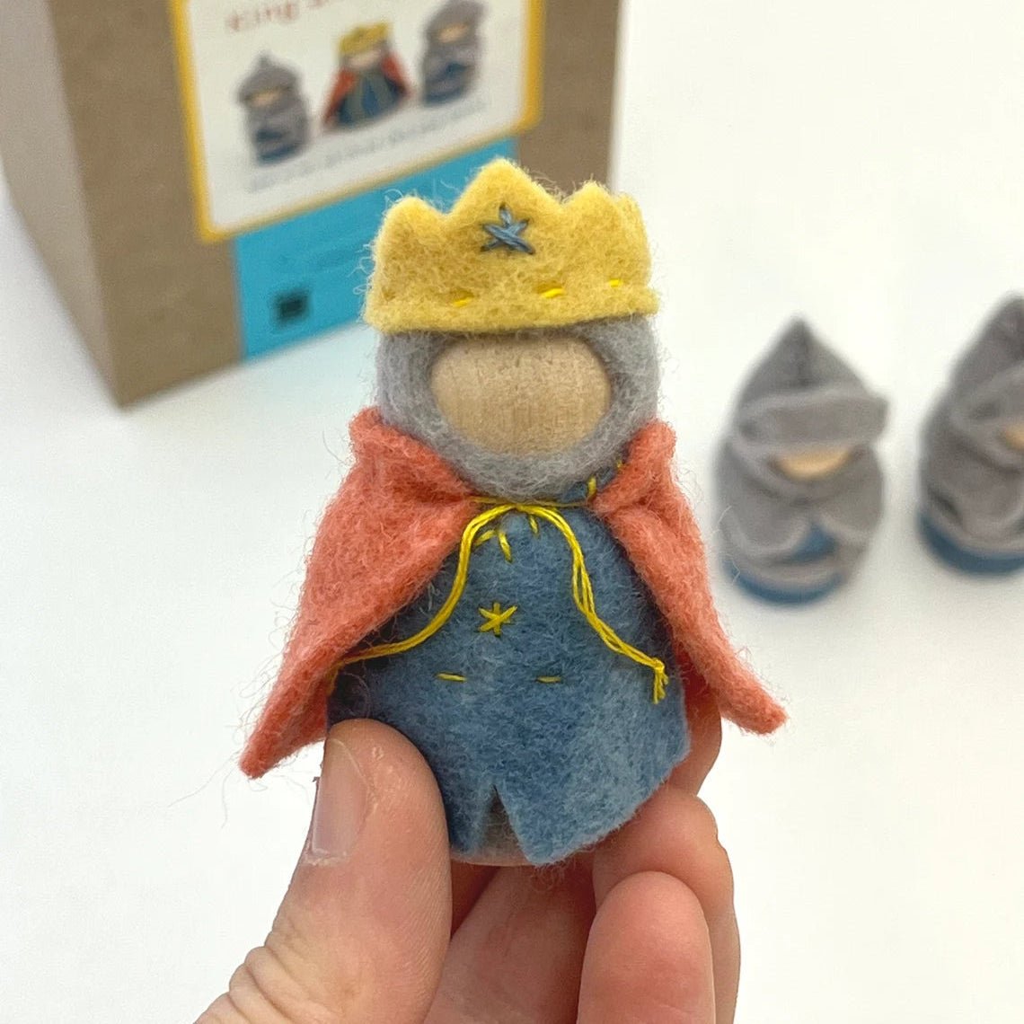 Small felt figurine of a king held by a hand, with a cardboard box in the background.