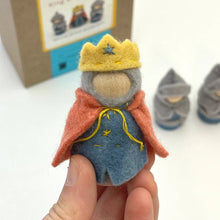 Small felt figurine of a king held by a hand, with a cardboard box in the background.