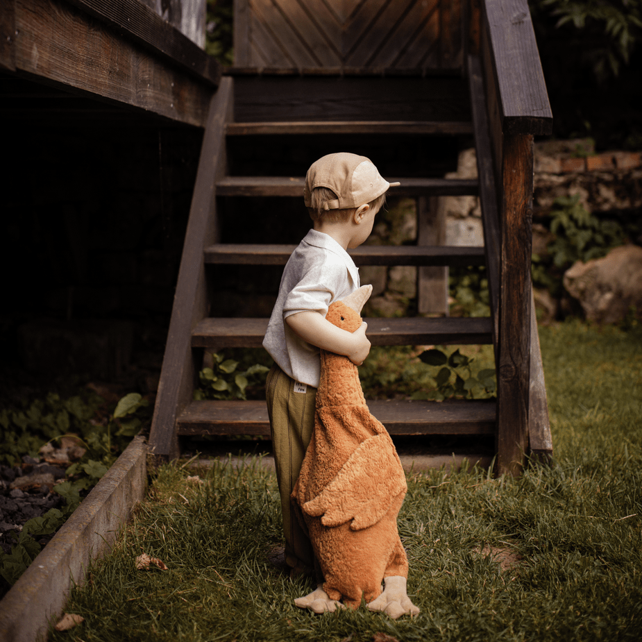 Child standing outside in front of wooden steps holding a rust-colored stuffed goose