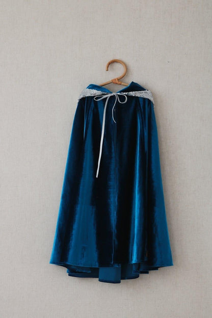 Deep blue velvet hooded cape with silver sequined hood and silver ribbon bow hanging on a wooden hanger