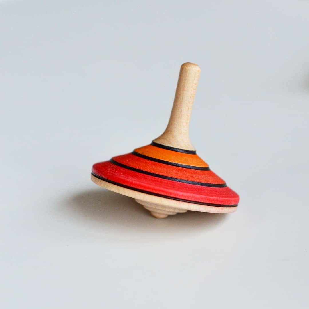 Wooden spinning top with red and orange striped design on a light gray background