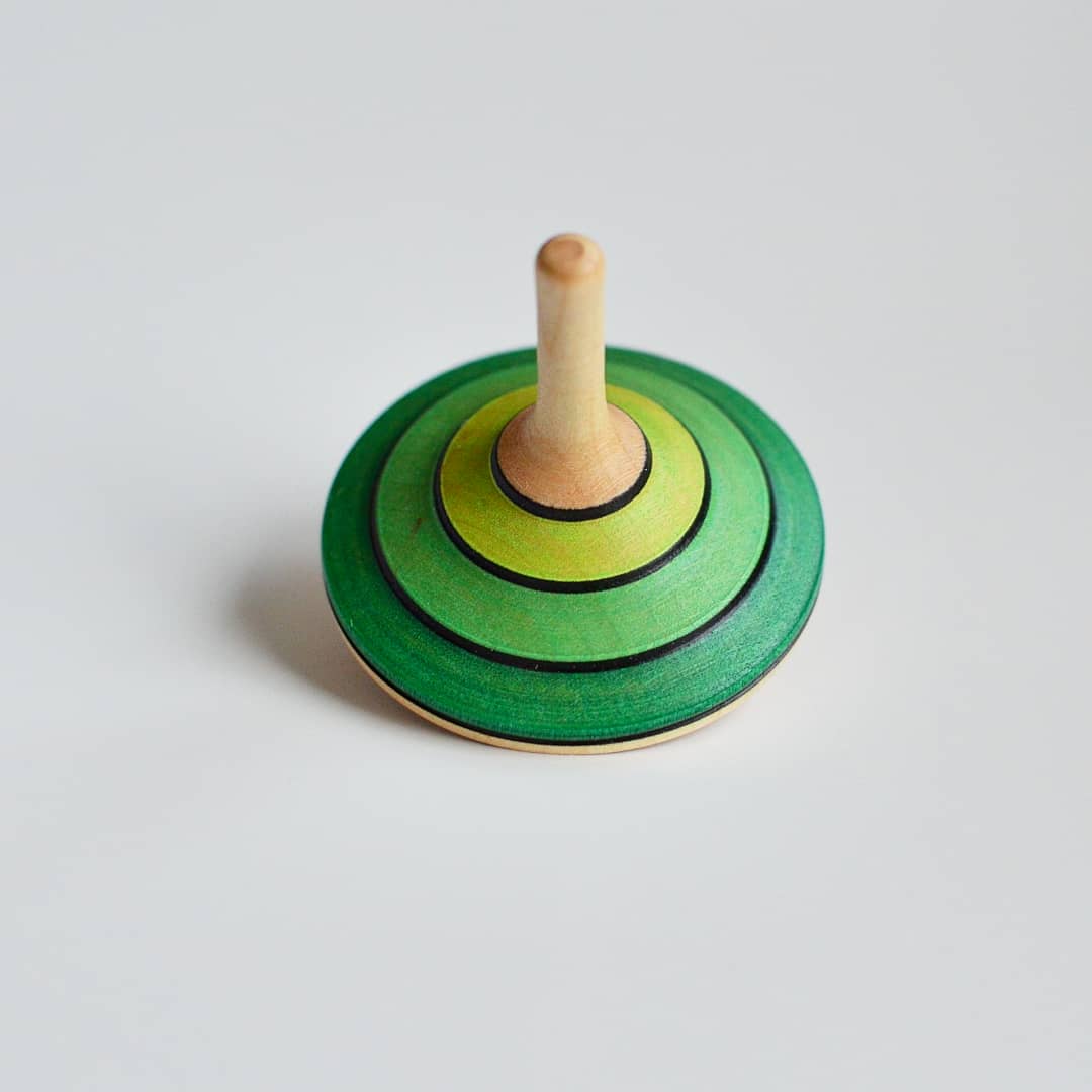 Wooden spinning top with green and yellow rings on a light gray background