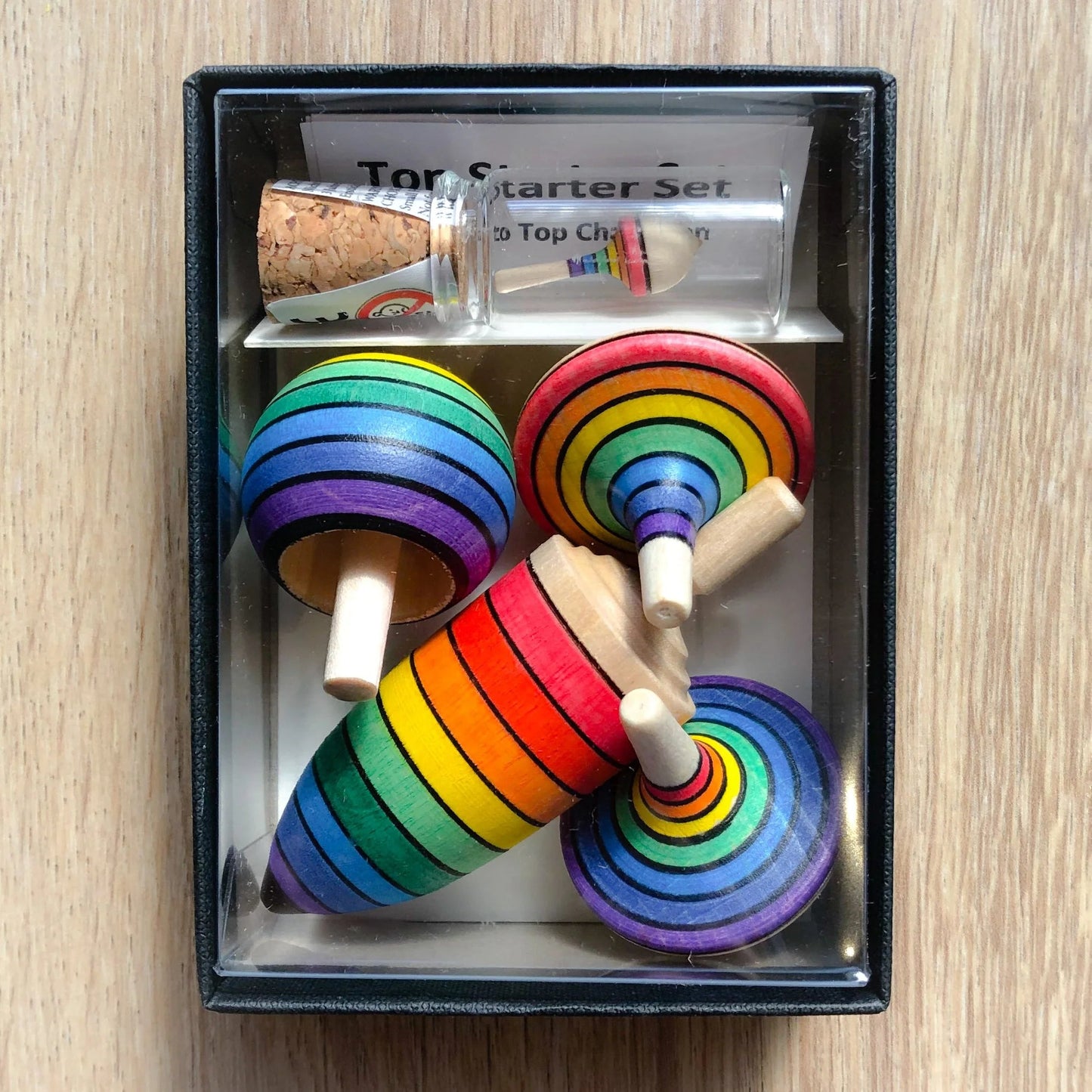 Set of rainbow-colored wooden tops in a box on a wooden surface