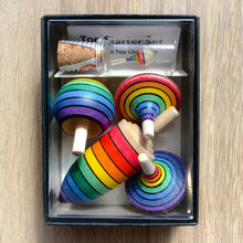 Set of rainbow-colored wooden tops in a box on a wooden surface