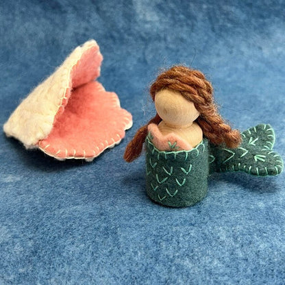 Small sewn mermaid figurine with a shell on a blue fabric background