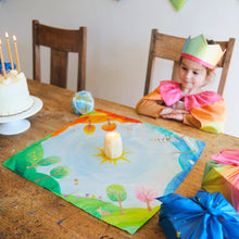 Child in a rainbow dress sitting at a table with a decorated cake and colorful seasonal playsilk with candle in the middle