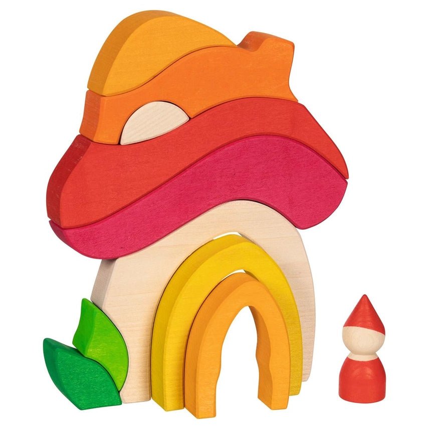 Wooden blocks in warm reds, yellows, and oranges arranged in a mushroom house shape, with a wooden gnome peg doll next to it on a white background.