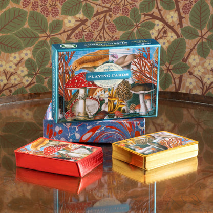 Playing card set with mushroom design packaging on a reflective surface.