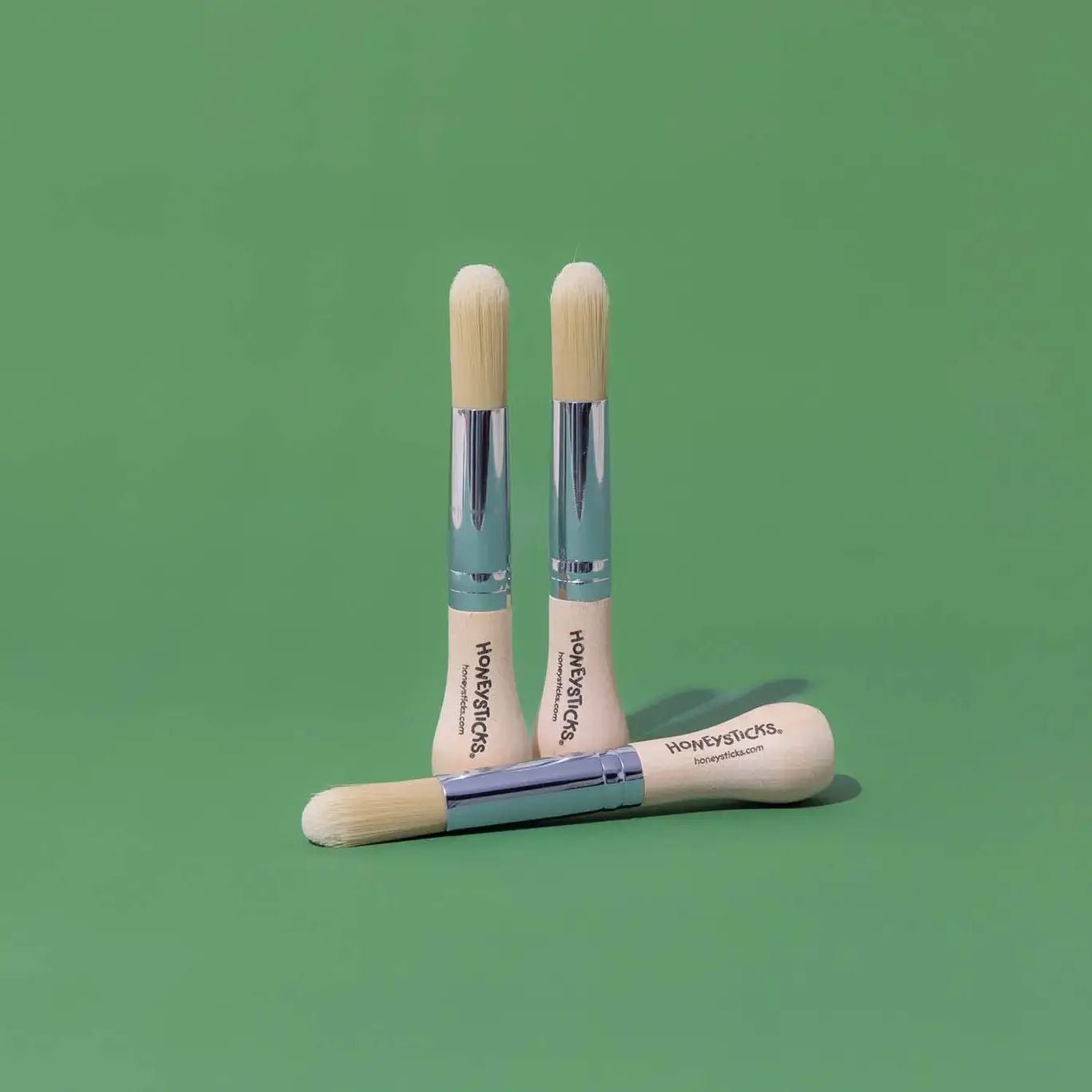 Three wooden paint brushes with silver tips on a green background