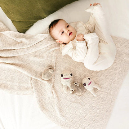 Baby laying on a bed with a green pillow and tan blanket next to two crocheted teeth-shaped and one mouse toy