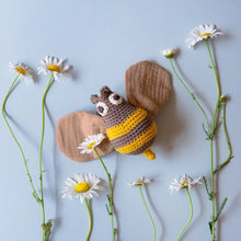 Crocheted bee toy surrounded by daisies on a light blue background