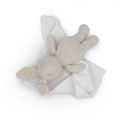 Crocheted bunny toy on a white blanket with a white background
