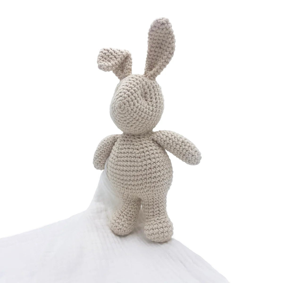 Crocheted bunny toy holding a white blanket on a white background