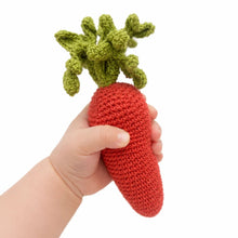 Baby's hand holding a crocheted carrot rattle against a white background