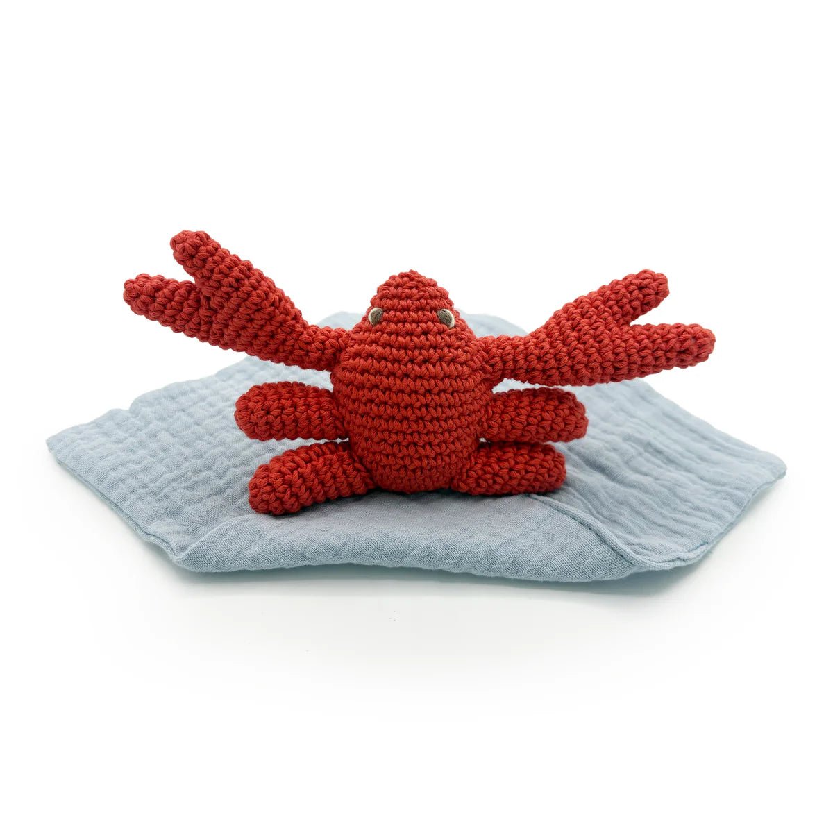 Red crocheted crab toy on a grey blanket with a white background
