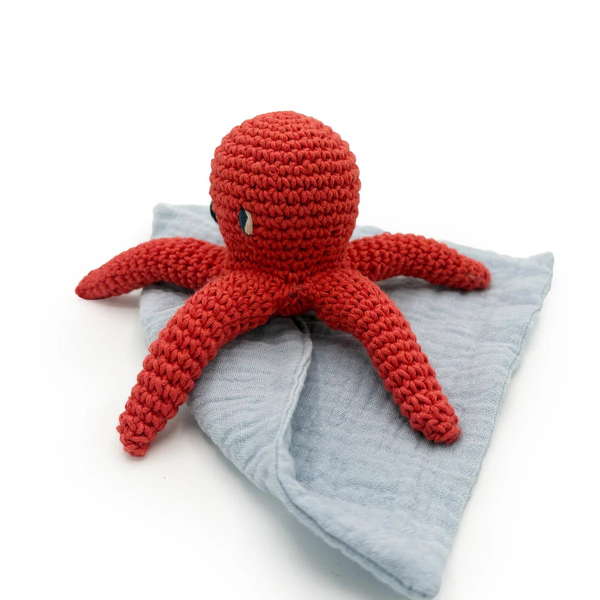 Red crocheted octopus toy on a gray blanket with a white background