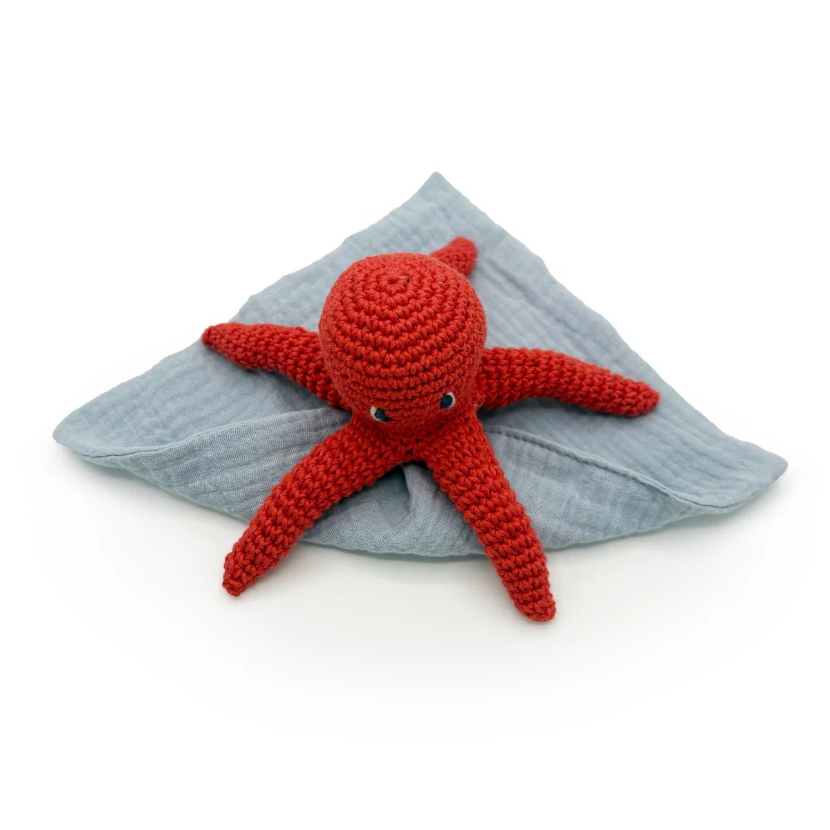 Red crocheted octopus toy on a grey blanket with a white background