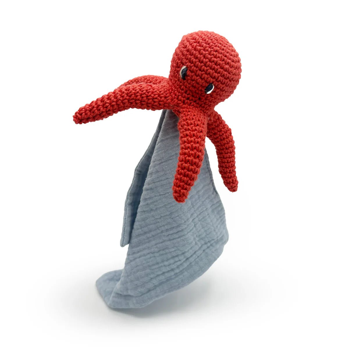 Red crochet octopus toy on a gray textured blanket against a white background