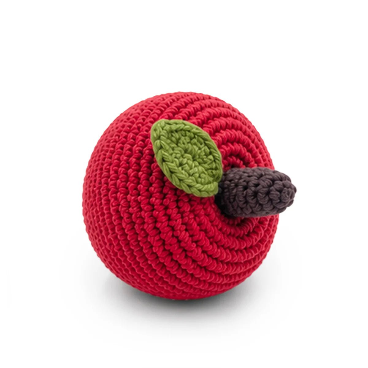 A crocheted apple rattel in bright red, with a green leaf and a dark brown stem, photographed on a clean white background.