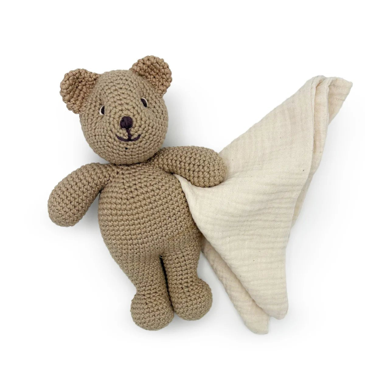 Crocheted teddy bear holding a beige blanket on a white background
