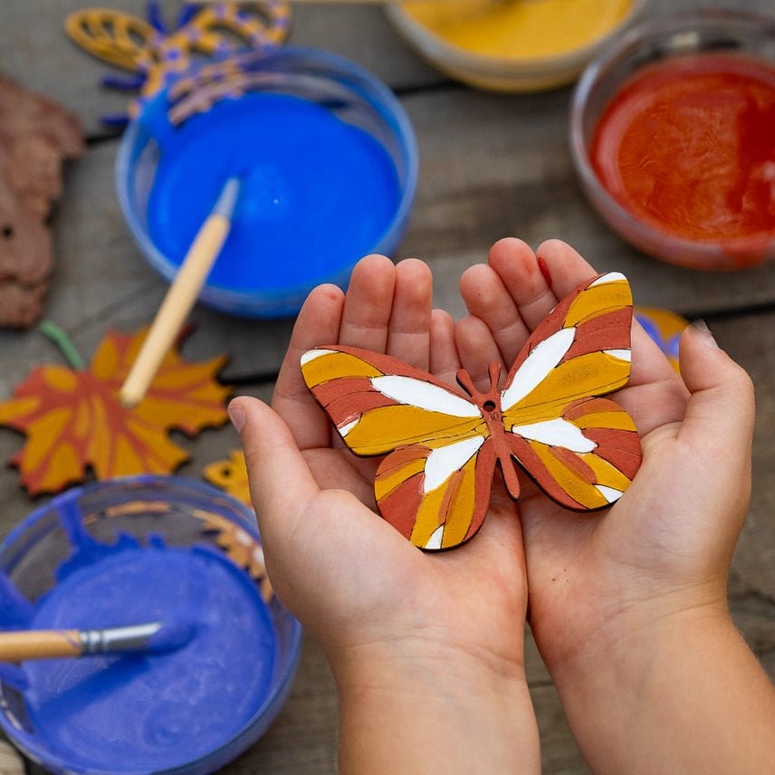 Child holding a painted butterfly craft with art supplies on a wooden surface