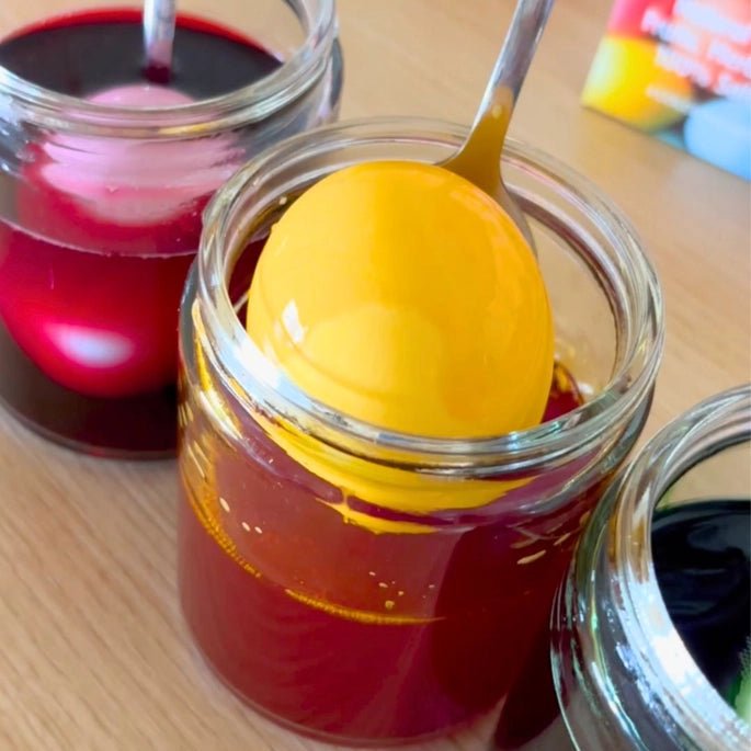 Yellow Easter egg in a glass jar with red liquid, on a wooden surface.