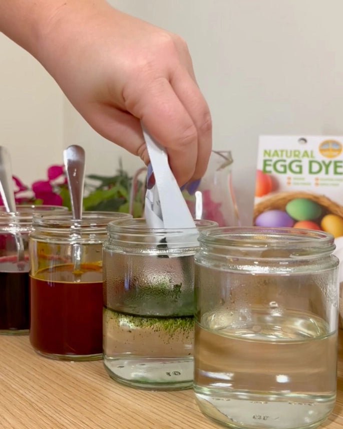Person preparing natural egg dye with jars of liquid on a table.