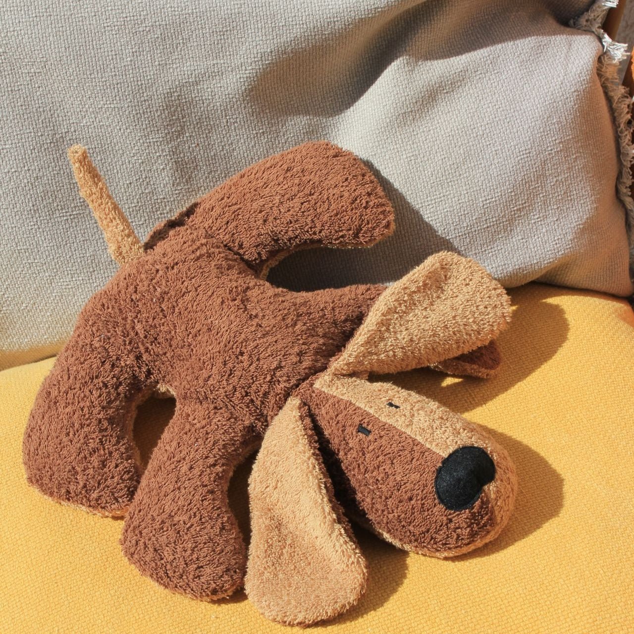 Brown plush dog toy on a yellow surface with a neutral background