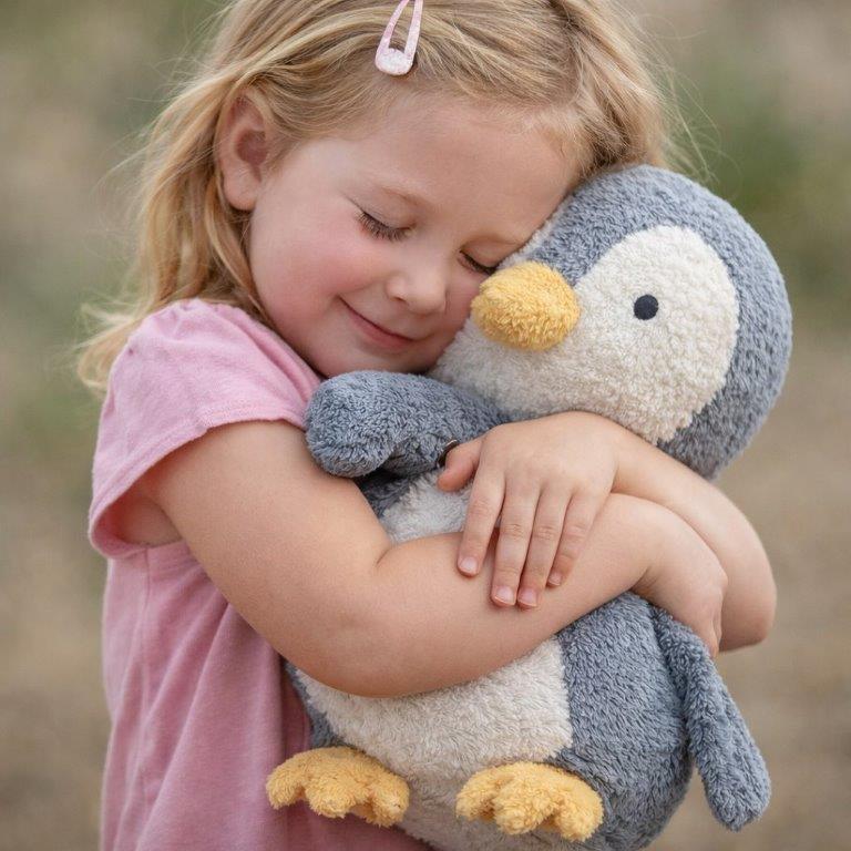 Young girl hugging a plush penguin toy outdoors