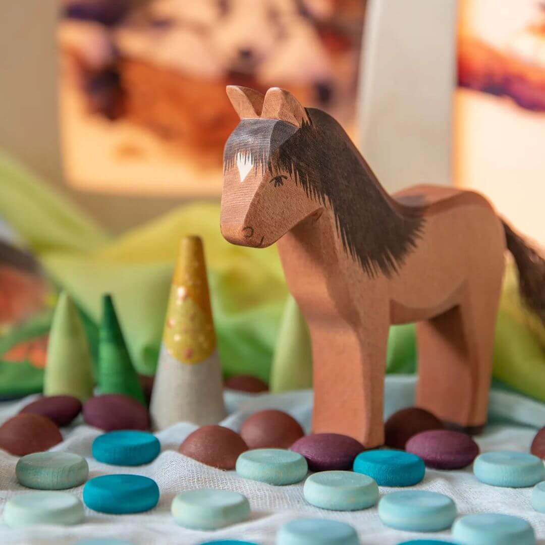 Brown wooden horse figurine amongst many colored open-ended play pieces
