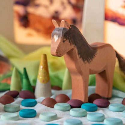 Brown wooden horse figurine amongst many colored open-ended play pieces