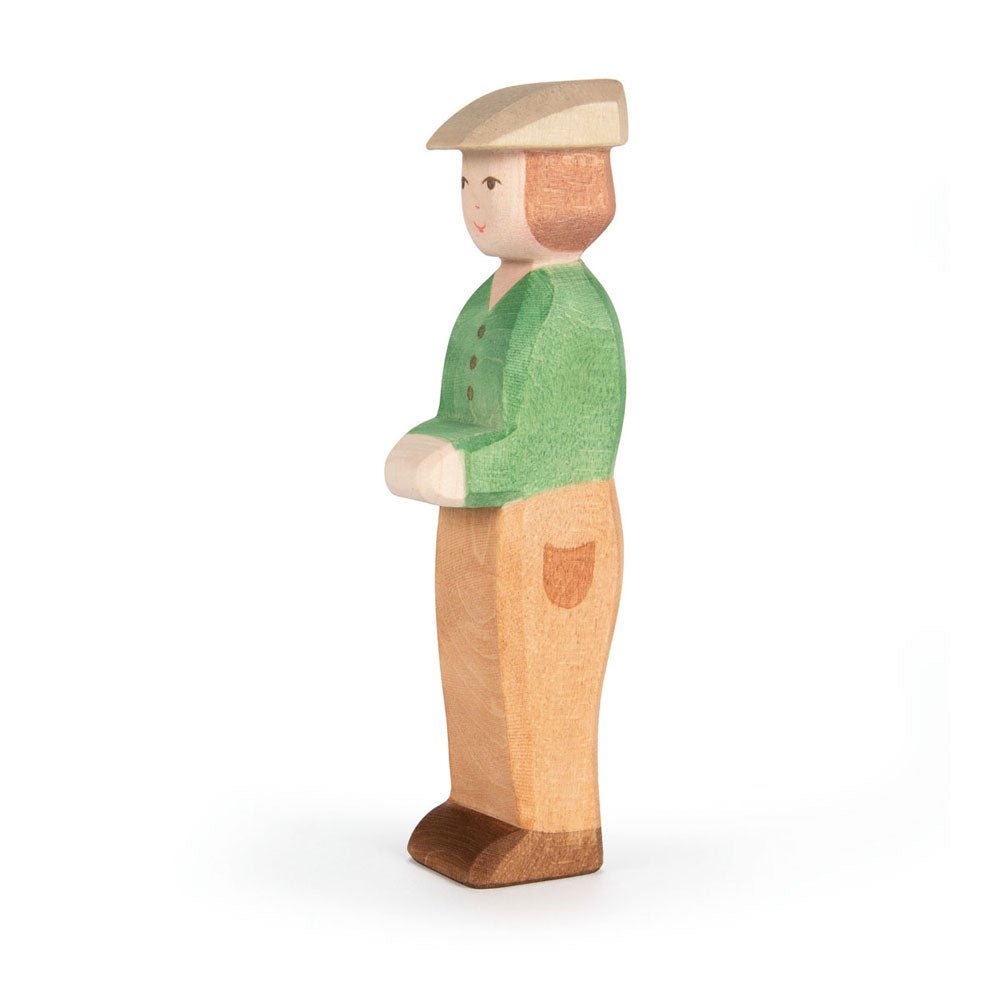 Wooden figure of a young boy with a green shirt and brown slacks on a white background
