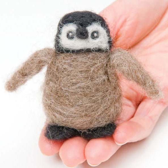 Hand holding a needle felted baby penguin on a white background