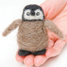Hand holding a needle felted baby penguin on a white background