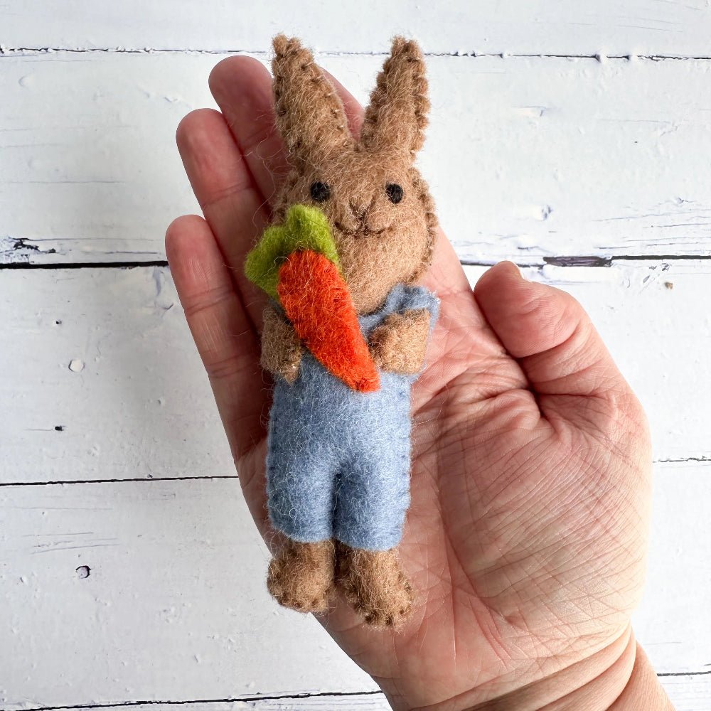 Small felt rabbit toy holding a carrot, held in a hand against a white wooden background
